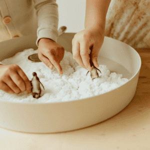 Handen spelen met witte Jellystone sensorische sneeuw en pinguïnfiguren in een ronde speelbak