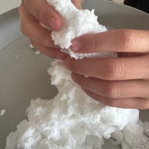 Close-up van handen die de zachte witte structuur van Jellystone Sensory Snow kneden