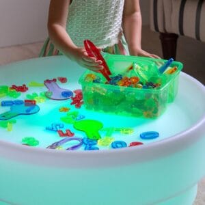 Kind sorteert transparante Tickit-vormen met een rode pincet op een lichttafel