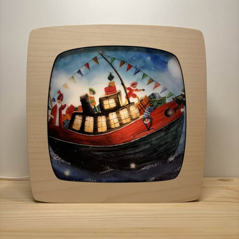 Toverplaat Bootje kadootje | Bijdehansje Toverplaat Bootje kadootje van Bijdehansje met Sinterklaas, cadeautjes en vlaggetjes op een boot, getoond in een houten seizoenenlamp
